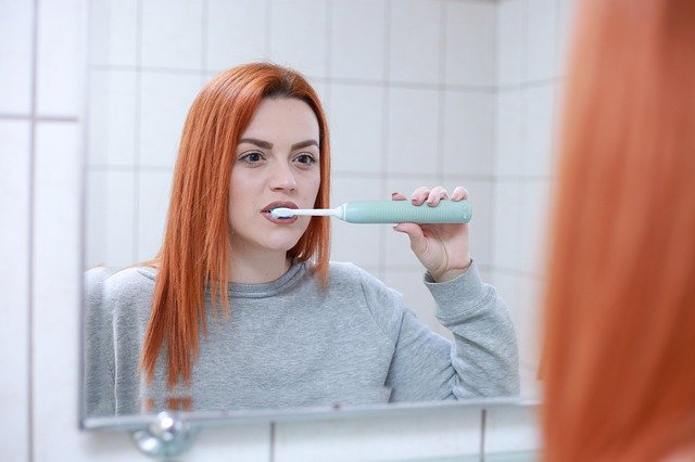 Mladá žena si čistí zuby před zrcadlem.